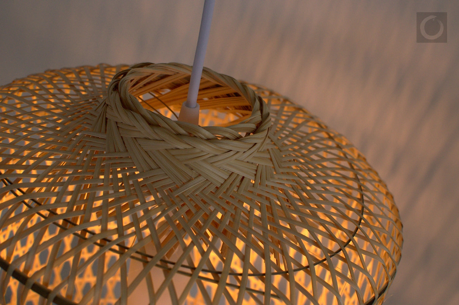 Closeup of a woven bamboo lampshade with a warm glow against a blurred background