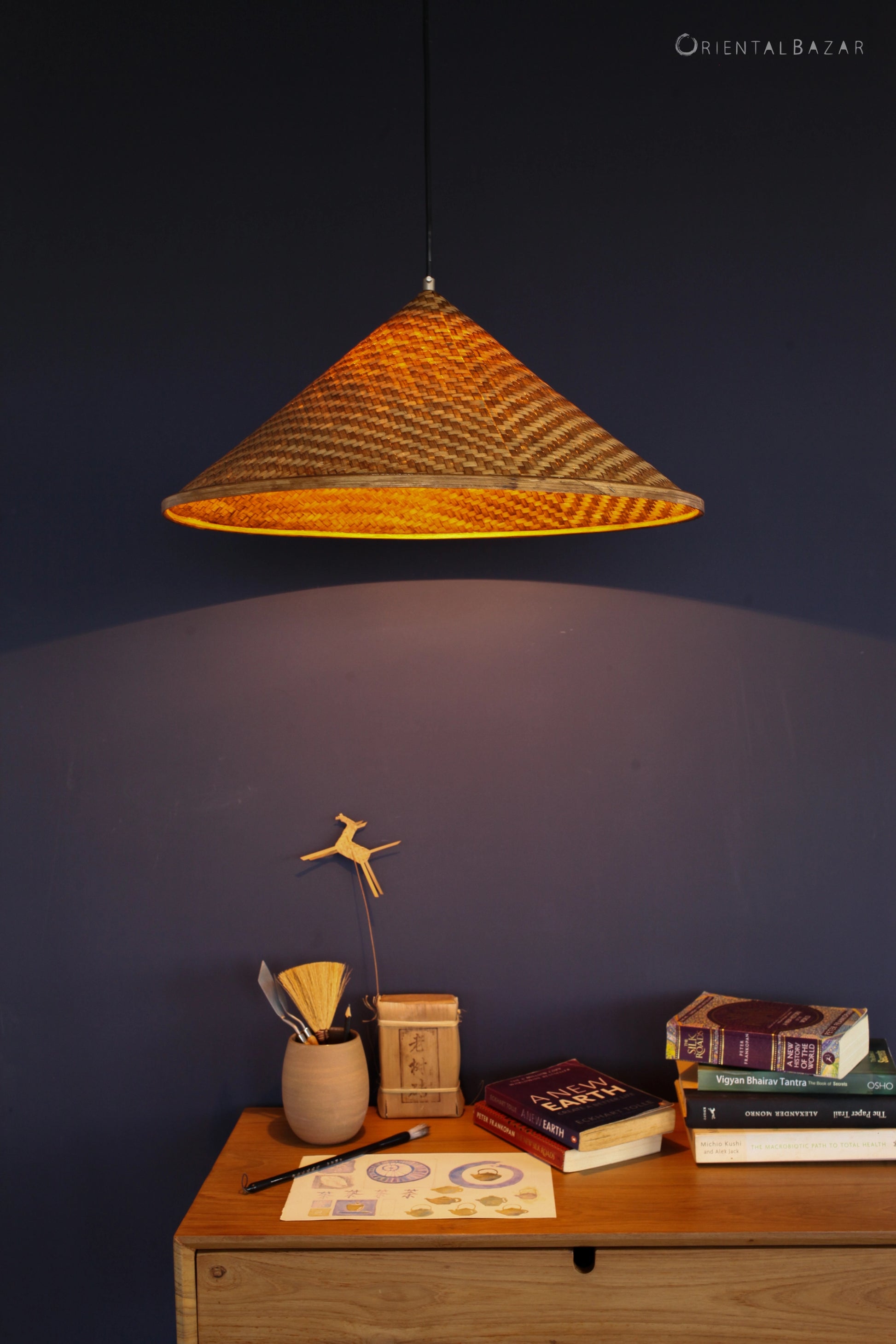 Bamboo pendant light hanging above a wooden surface with books and decorative items against a dark blue wall.