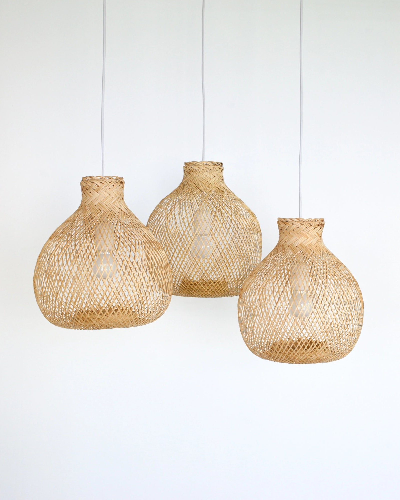 Three organic modern woven bamboo pendant lights hanging against a white background