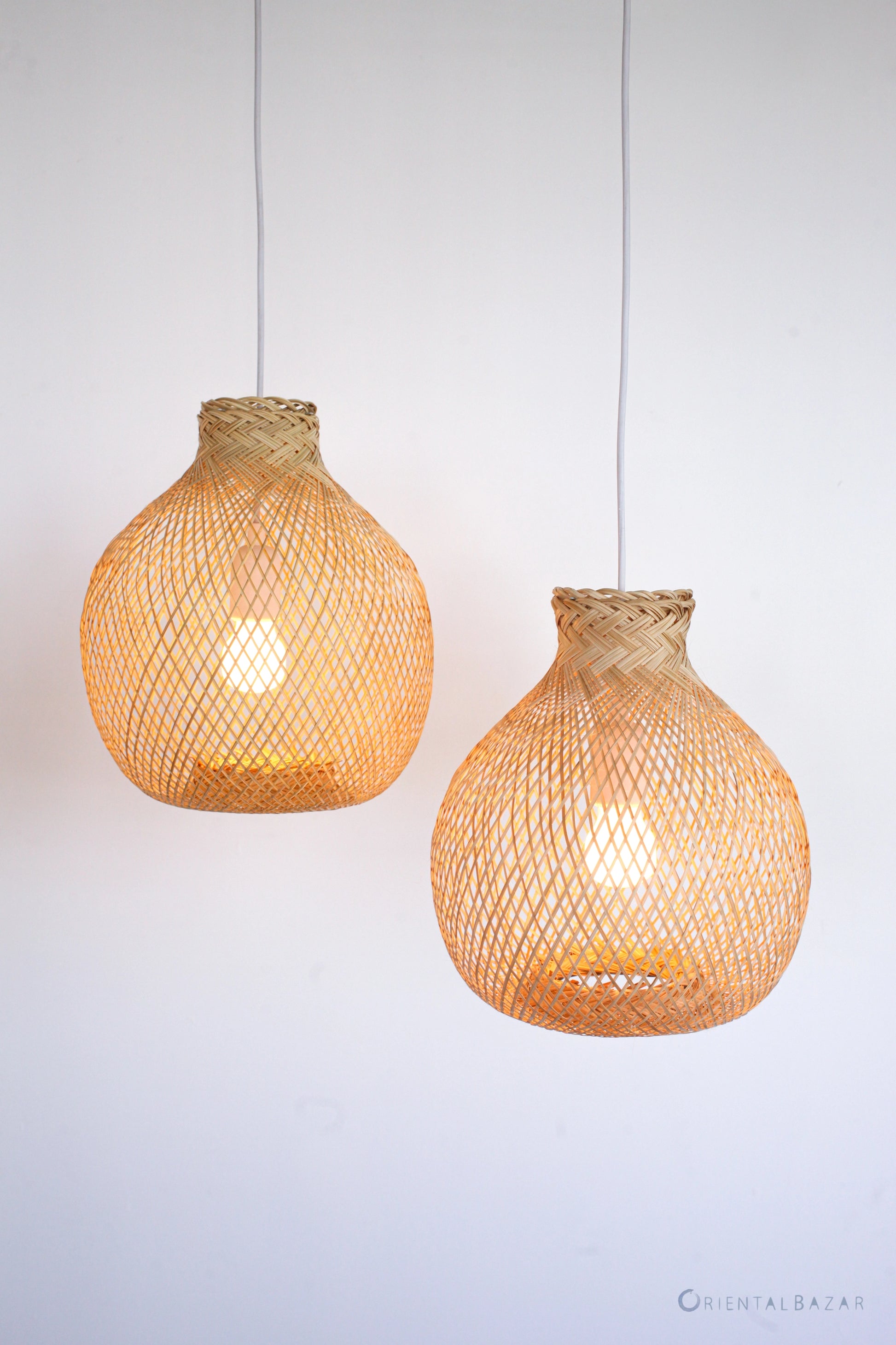 Two woven bamboo pendant lights hanging against a plain background