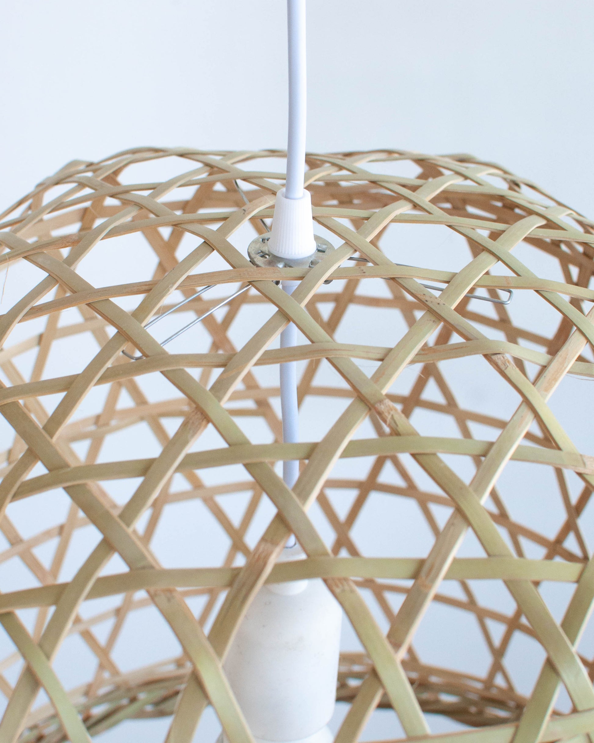 Close-up of a woven bamboo lampshade with a white ceiling fixture on a white background