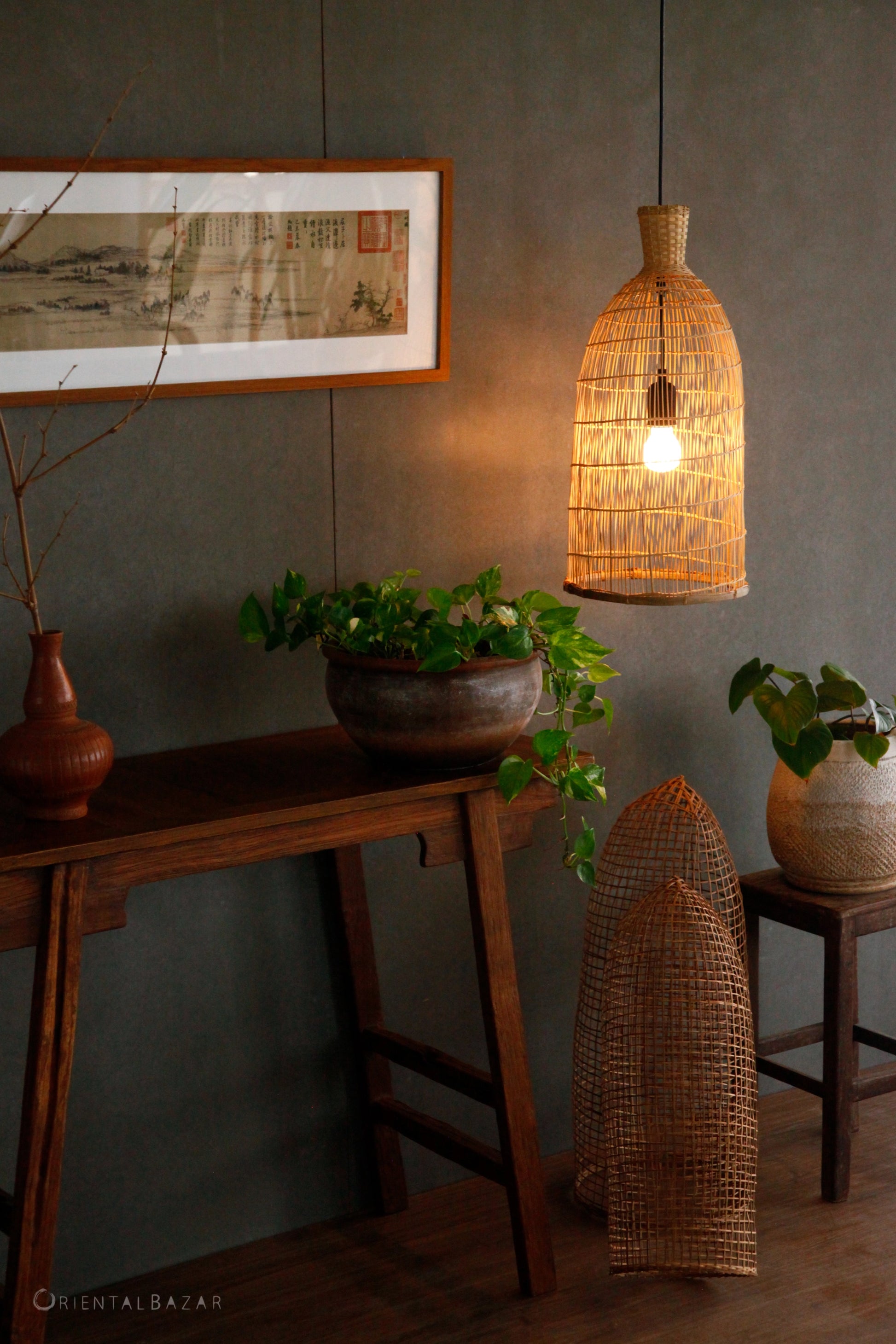 Woven bamboo pendant light hanging above a wooden console table with plants and natural decor