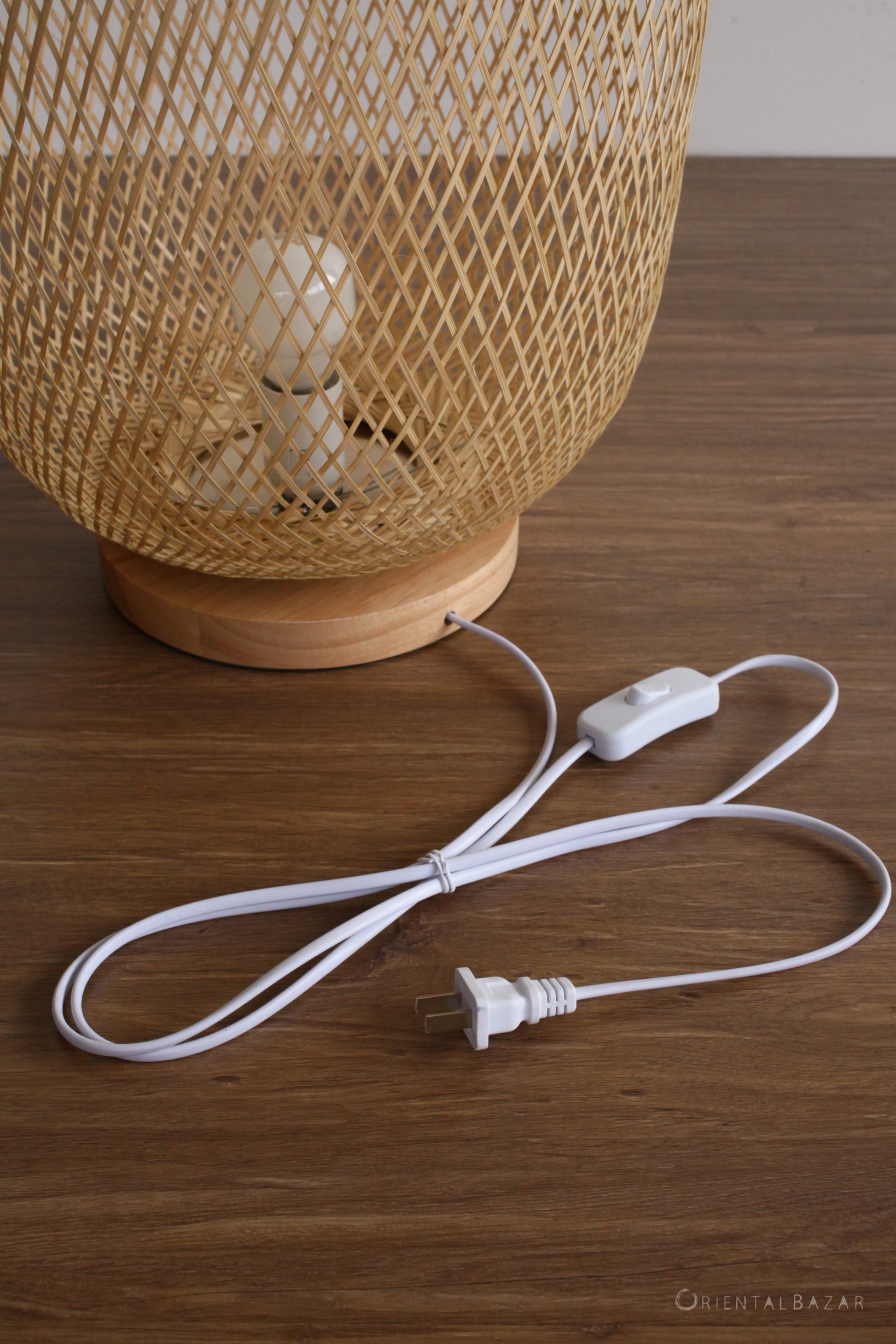 Woven bamboo lampshade with a white plug-in cord on a wooden surface