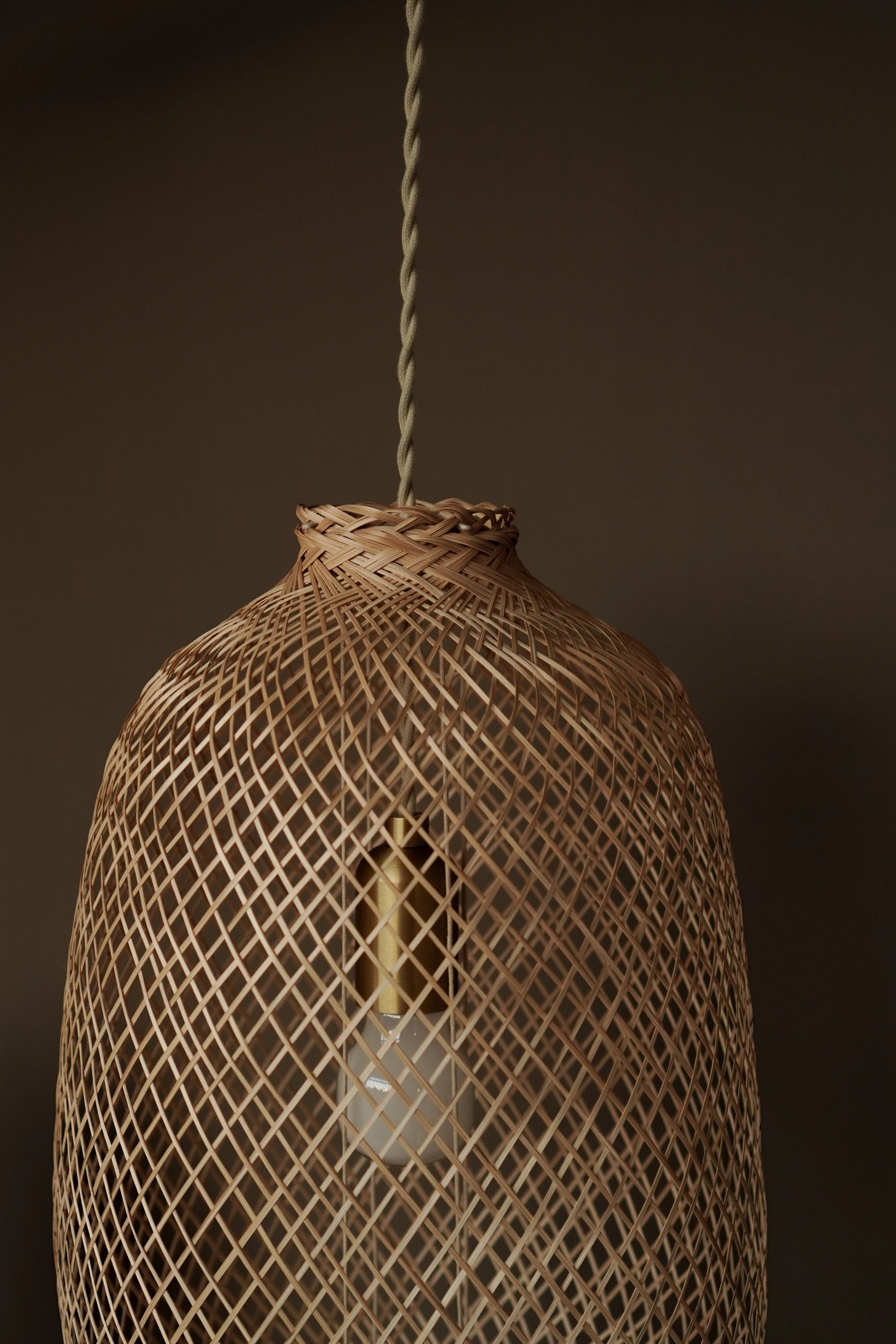 Woven bamboo light fixture with premium cord set and a bulb inside against a dark taupe background
