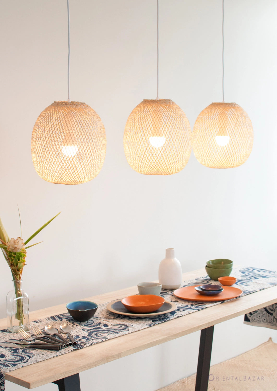 Three round woven bamboo pendant lights hanging above a dining table with a decorative tablecloth.
