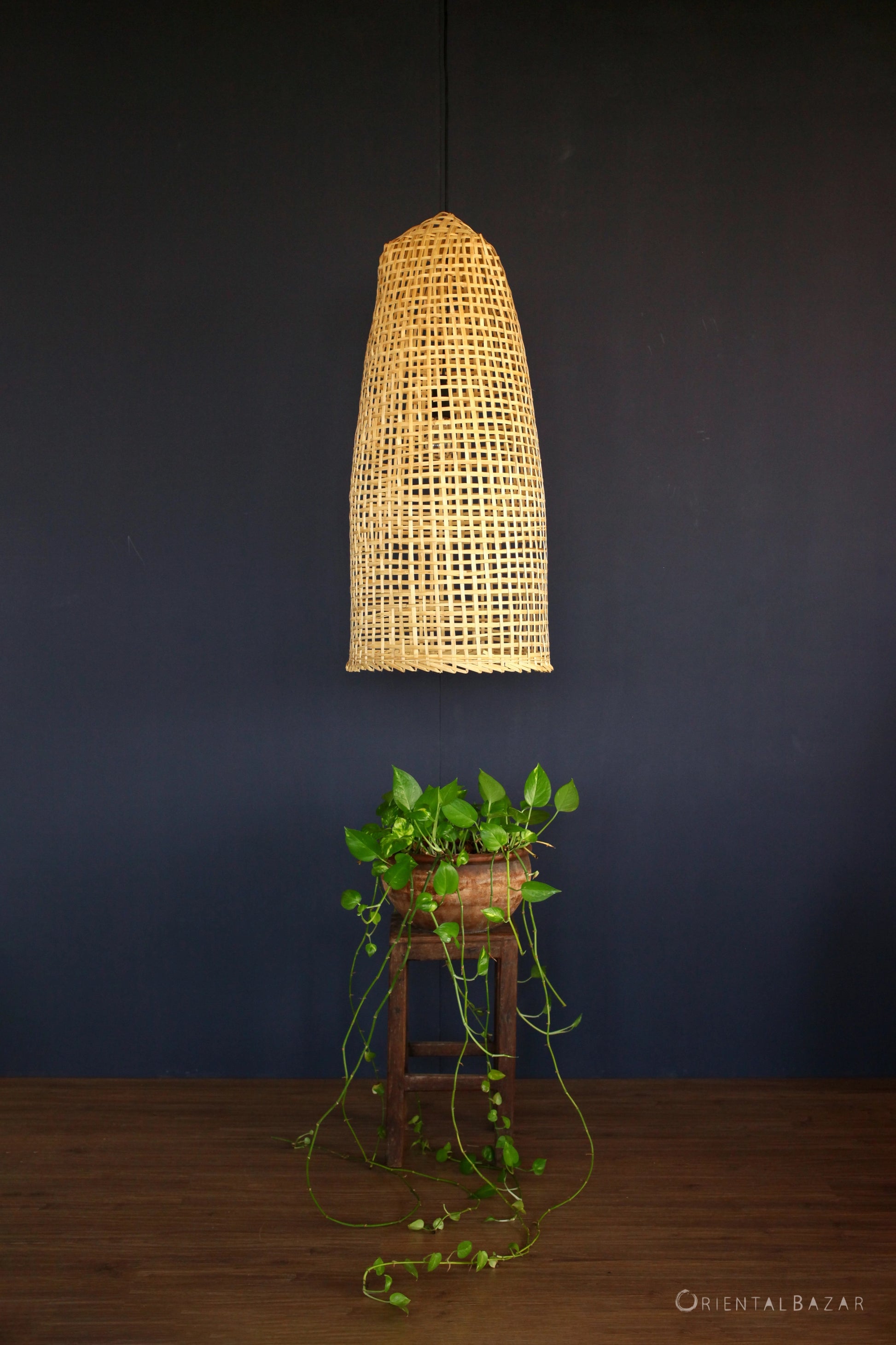 Woven bamboo ceiling light fixture on a dark wall with a plant below