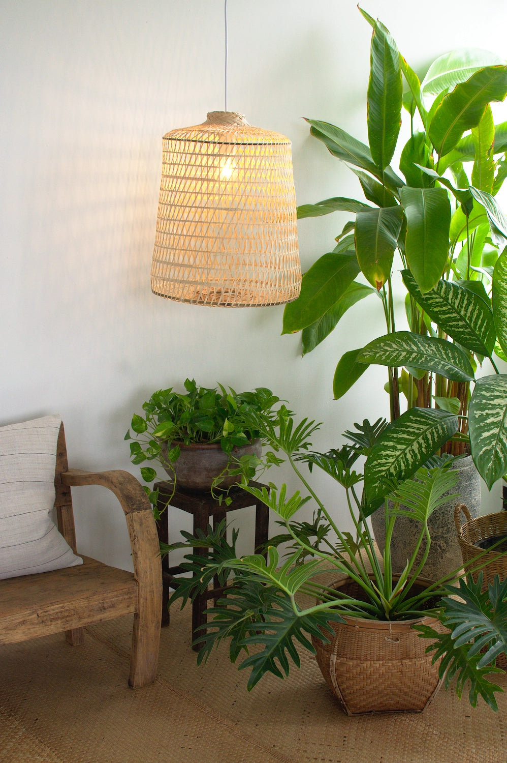 Indoor setting with a woven bamboo pendant light, wooden bench, and potted plants.