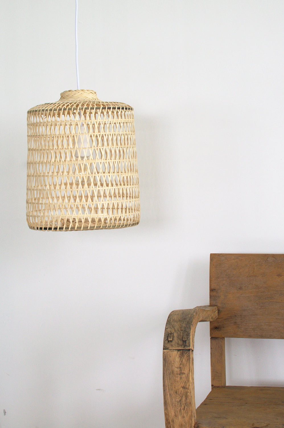 Boho bamboo lampshade hanging above a wooden chair against a white wall