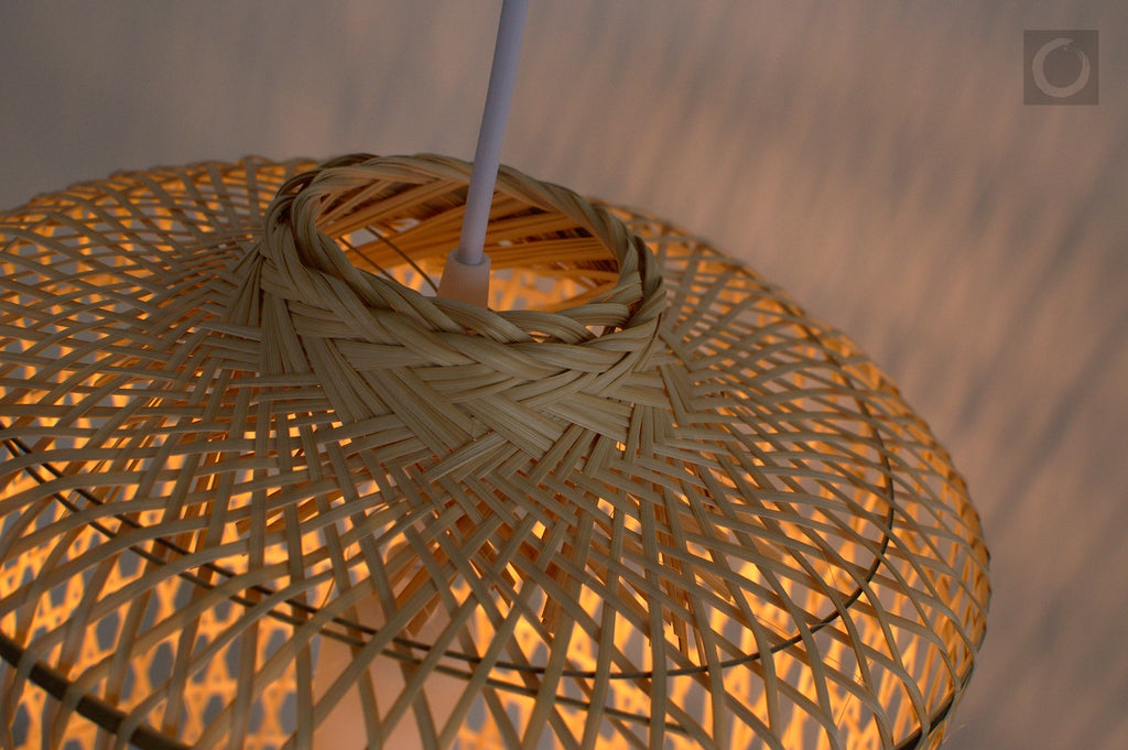 Closeup of a woven bamboo lampshade with a warm glow against a blurred background
