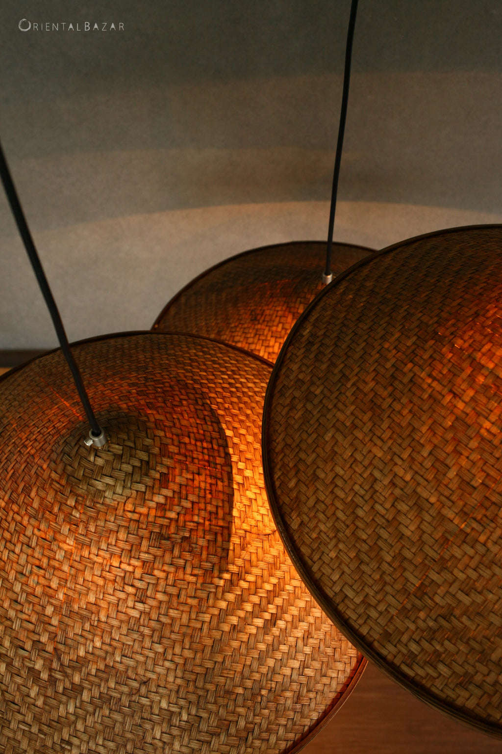 Close-up of woven bamboo pendant lights with a warm glow on a neutral background.
