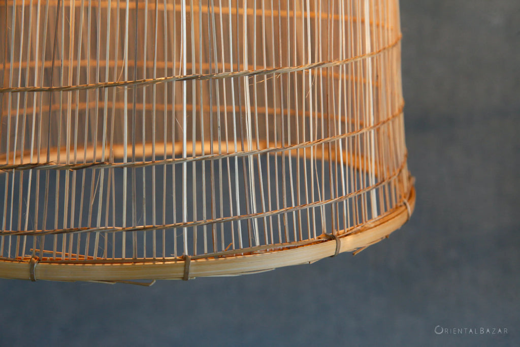 Closeup of the bottom rim of a bamboo fish-trap lamp showing the bamboo strips and rattan ties against a gray background