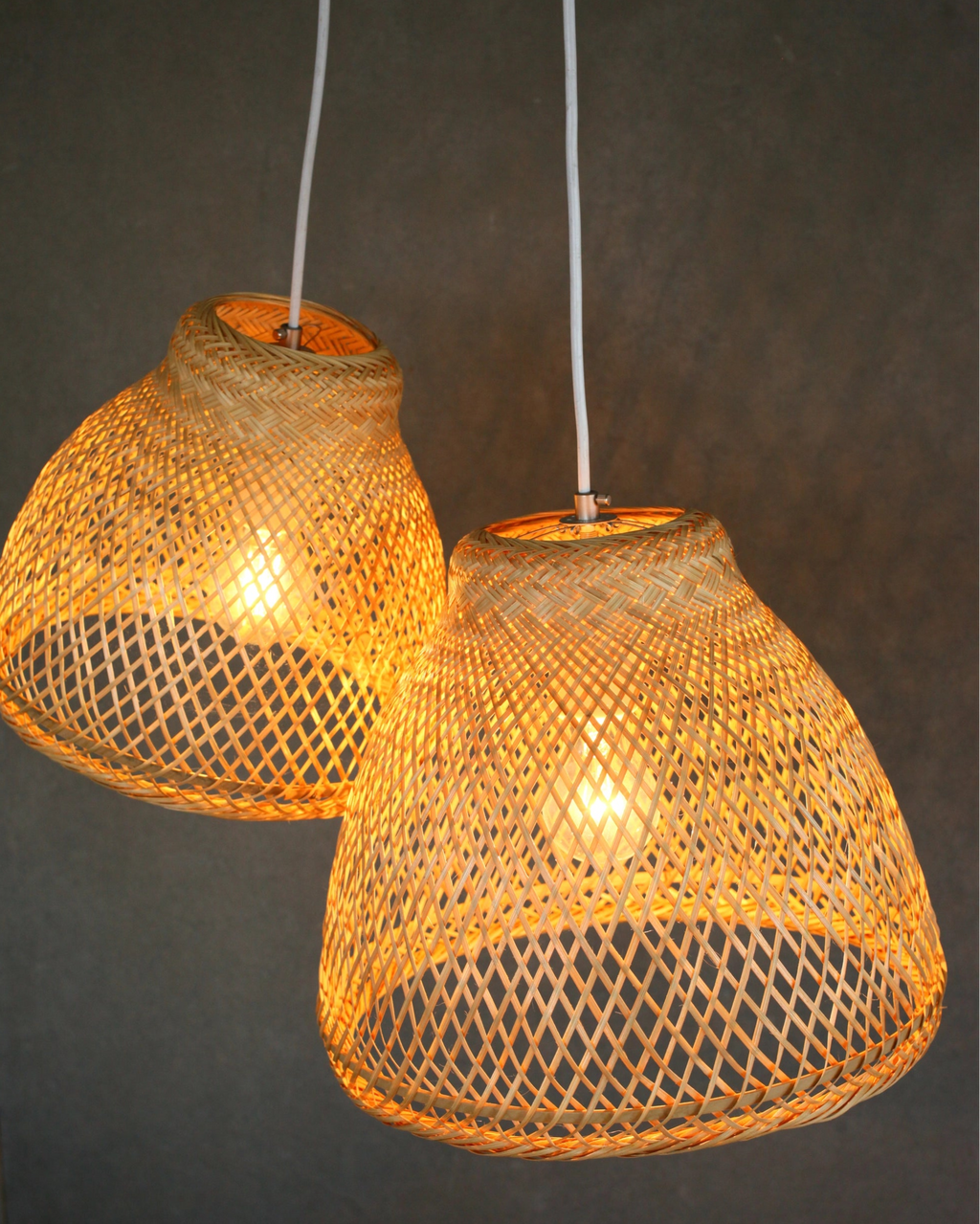 Two woven bamboo pendant lights glowing a warm light on a dark background with 