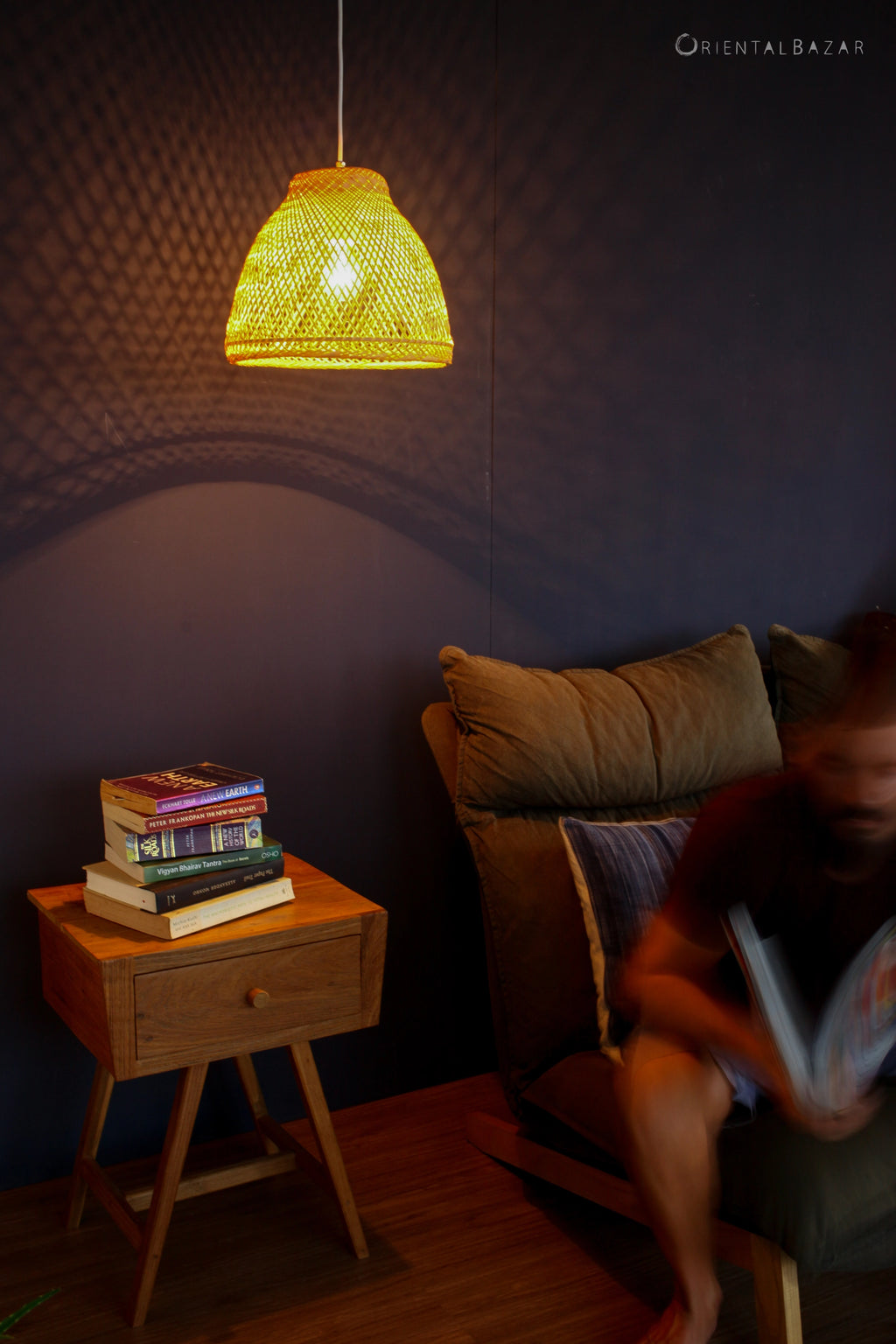 Living room with a woven bamboo pendant light, stack of books on a side table, and person reading