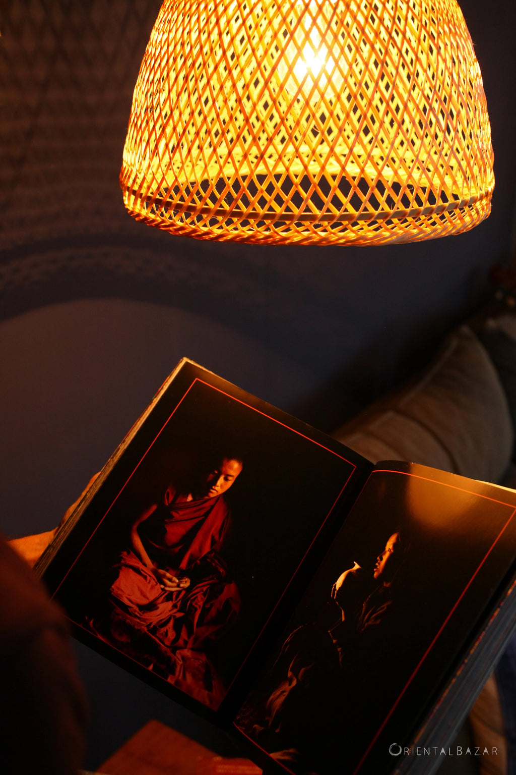 An open book with photographs of a Buddhist monk under a woven bamboo lampshade in a dimly lit room
