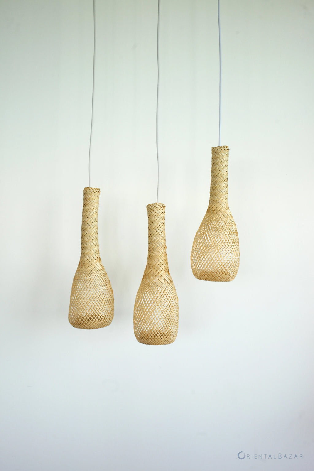 Three woven bamboo pendant lights hanging against a plain background