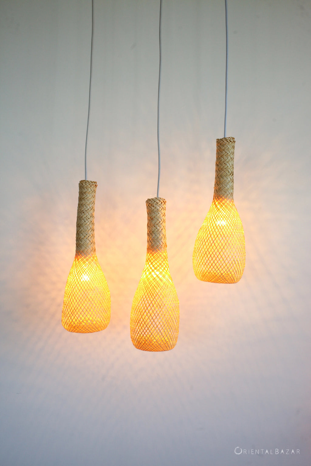 Three woven pendant lights hanging against a plain background and glowing warm light