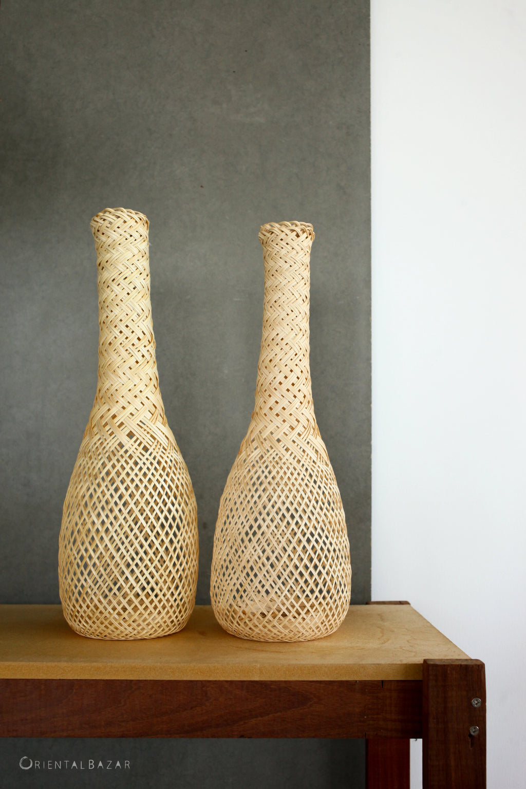 Two woven bamboo basket lamps on a wooden table against a gray wall.