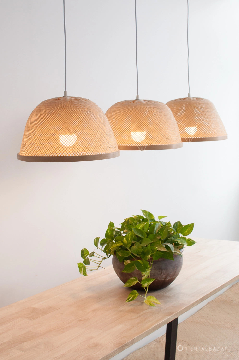 Three bamboo pendant lights hanging above a wooden table with a plant.
