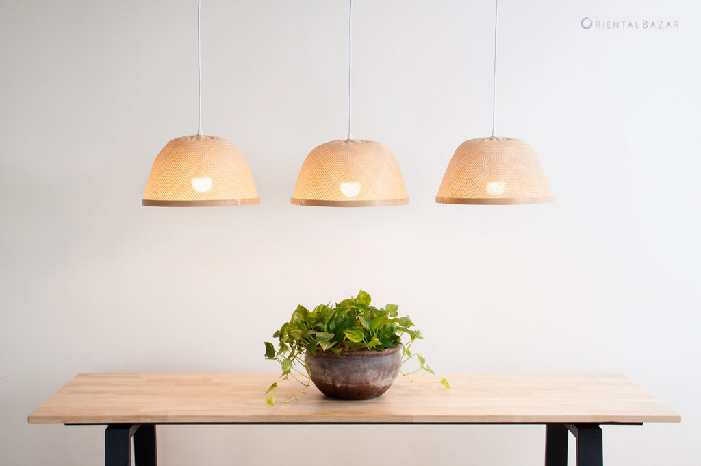 Three bamboo pendant lights hanging above a table with a plant on a plain background