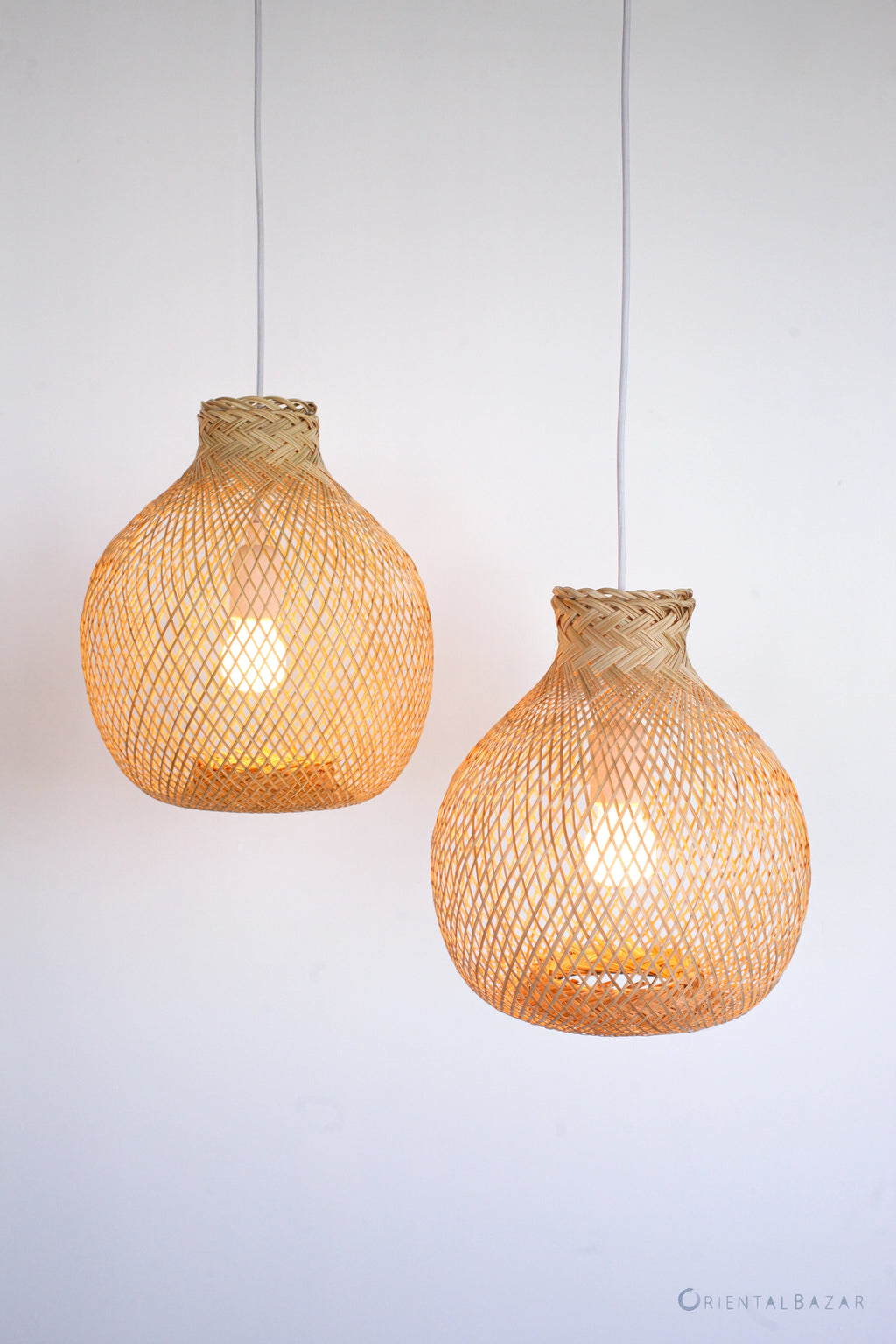 Two woven bamboo pendant lights hanging against a plain background
