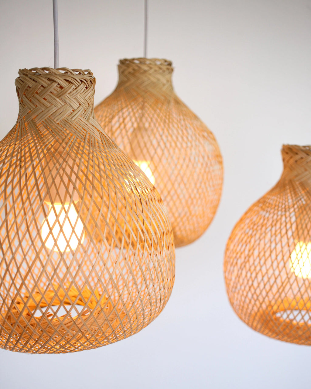 Three wabi-sabi woven bamboo pendant lights hanging against a white background