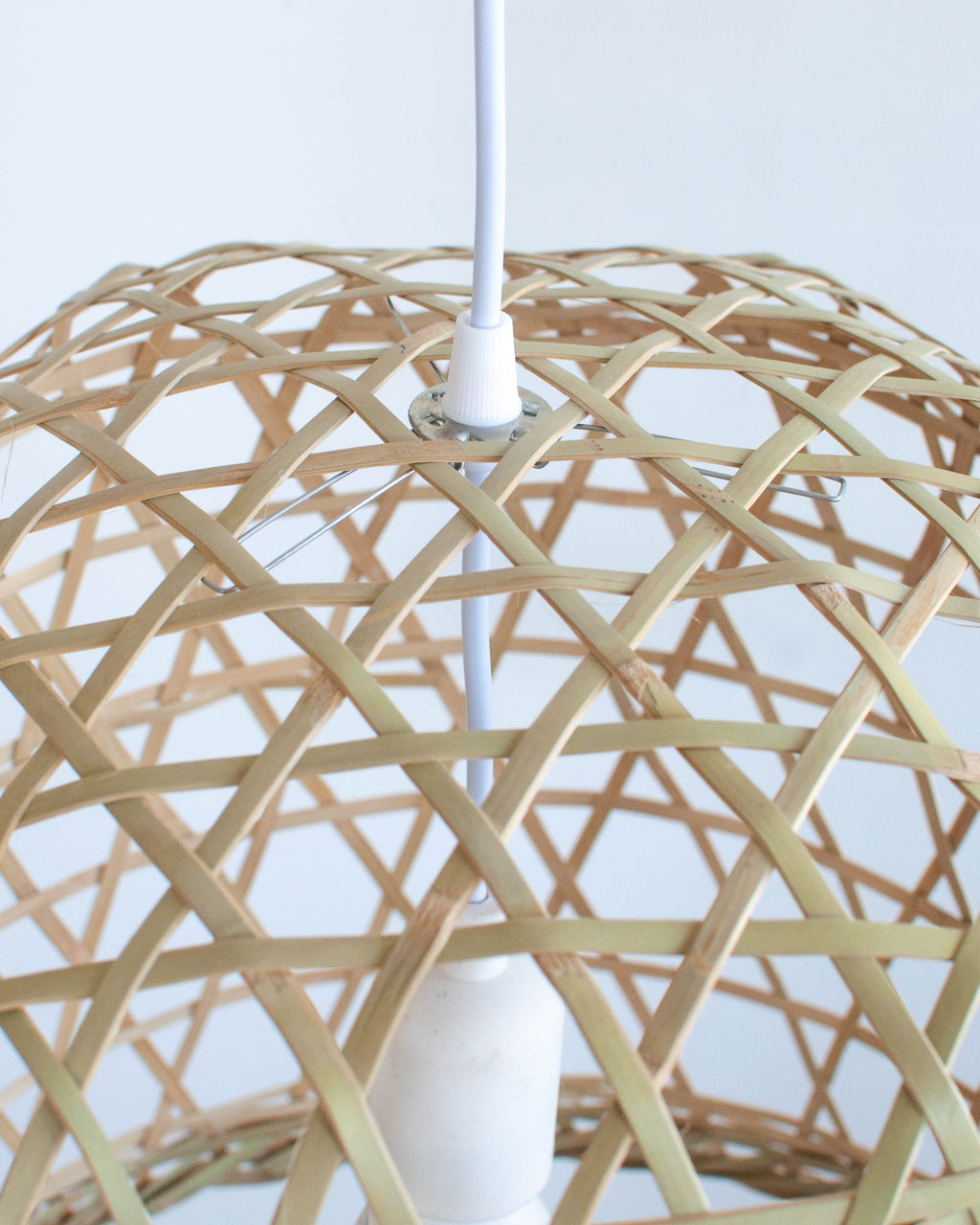 Close-up of a woven bamboo lampshade with a white ceiling fixture on a white background