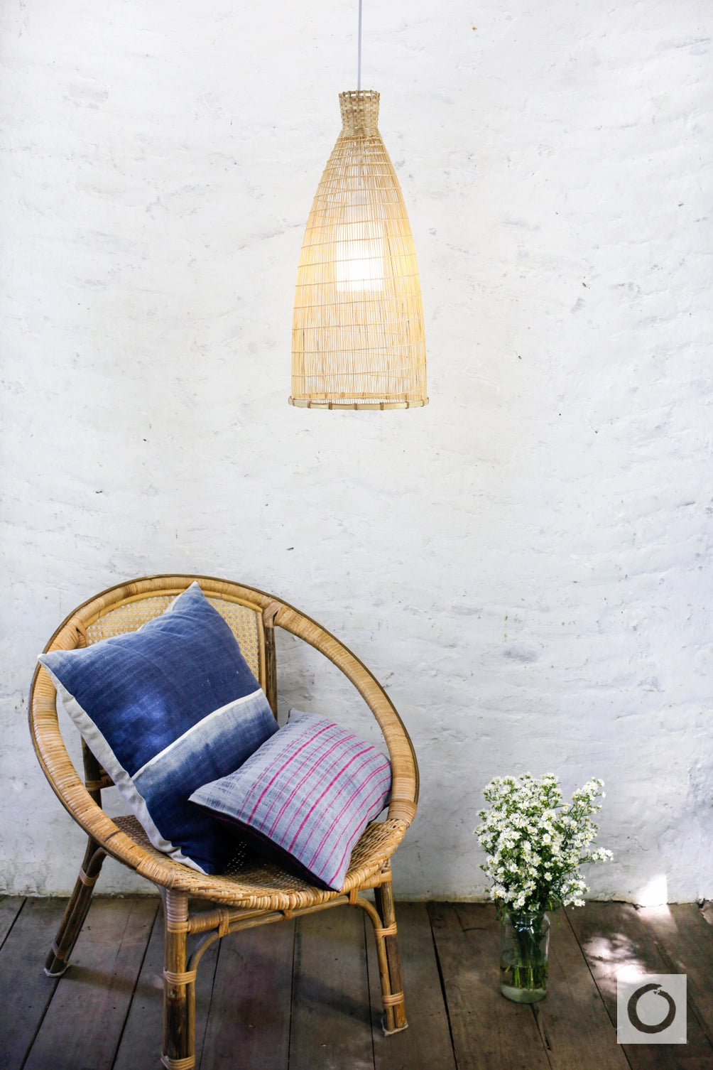Wicker chair with cushions and a hanging woven bamboo lamp against a white wall