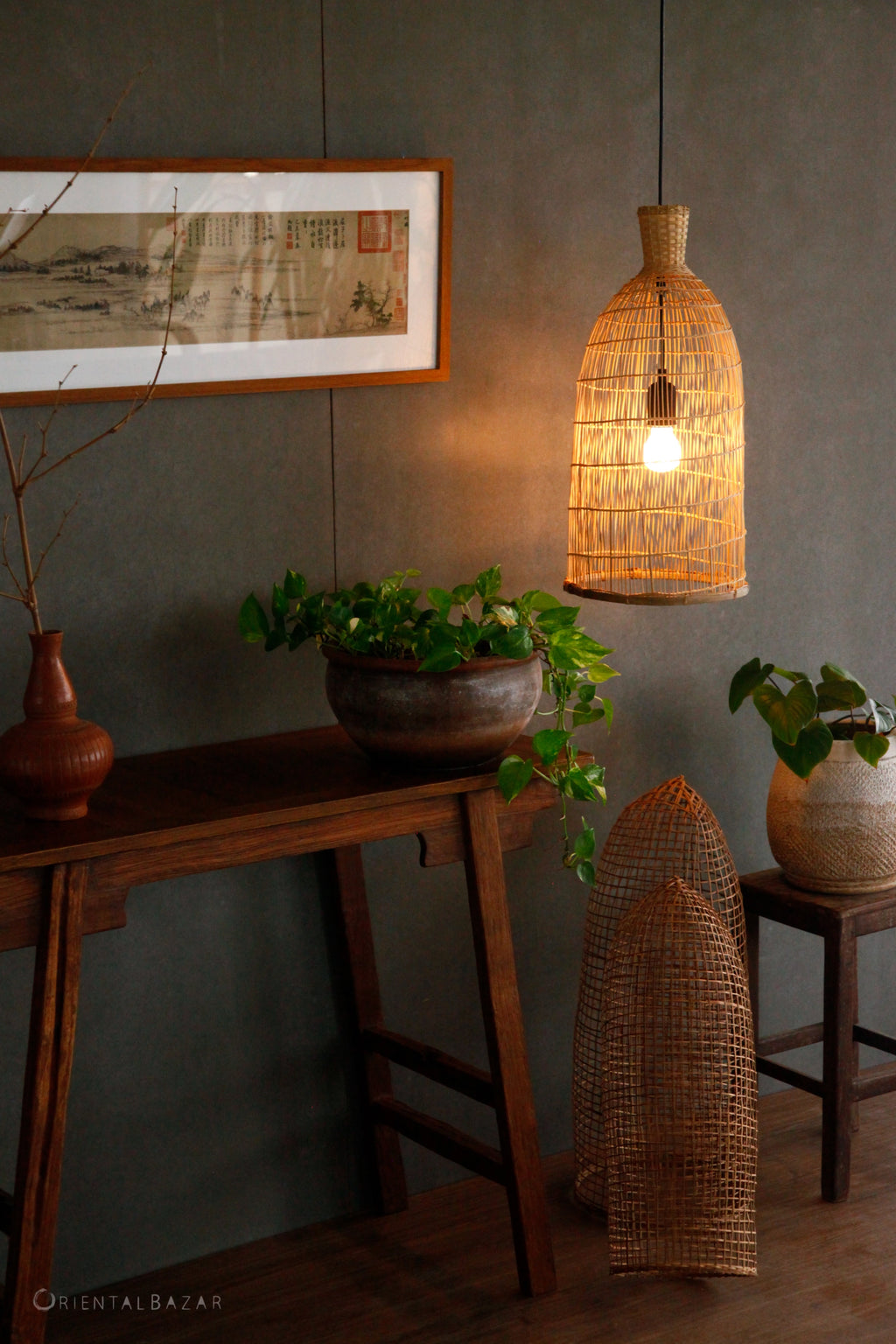 Woven bamboo pendant light hanging above a wooden console table with plants and natural decor