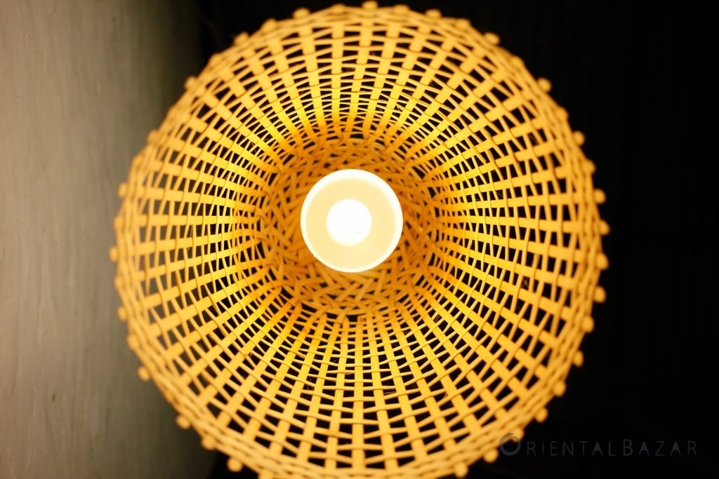Under view of a woven bamboo lampshade with a warm glow against a dark background