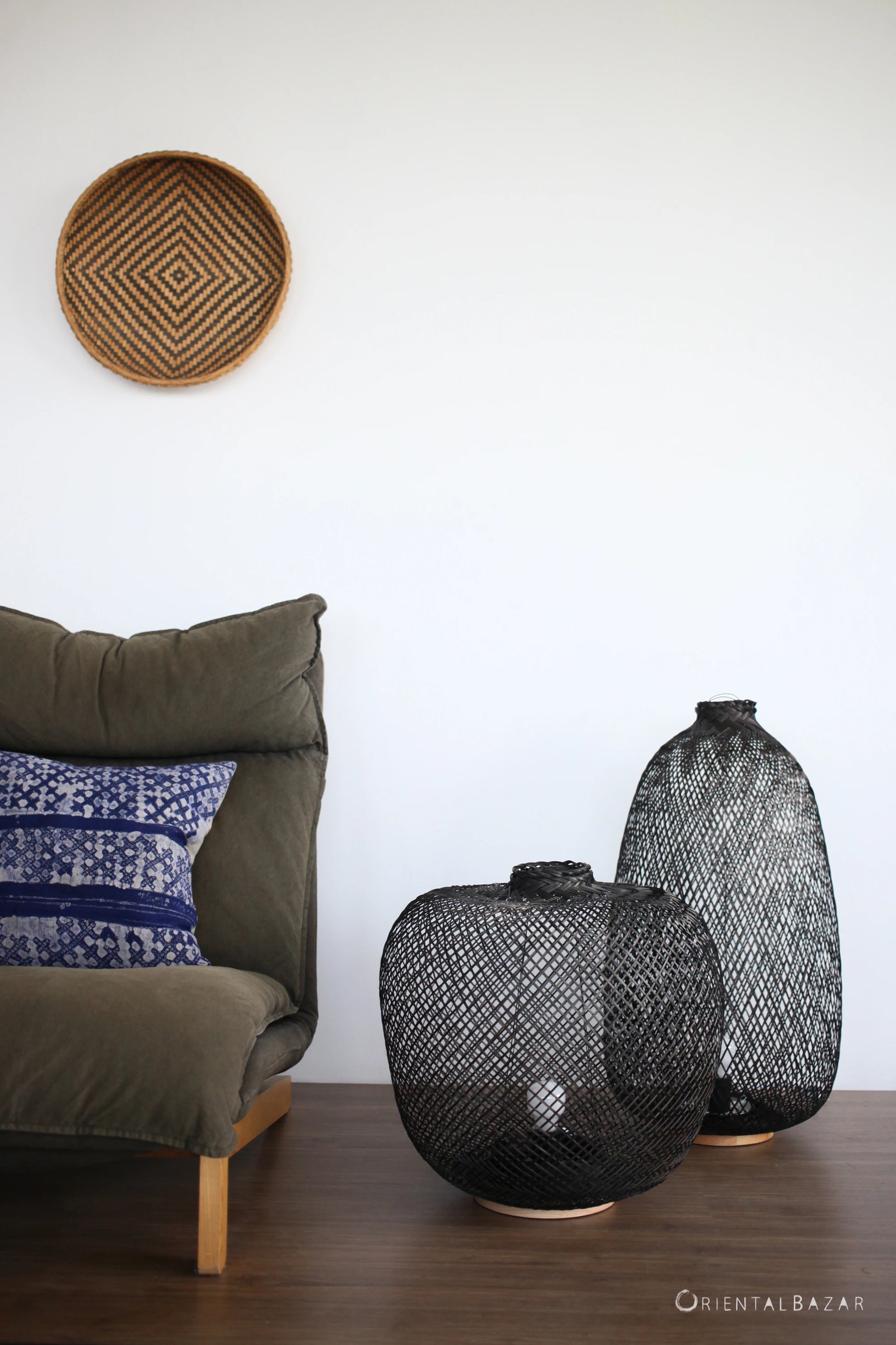 Black woven bamboo floor lamps on a wooden floor with a cushioned chair and wall art in the background.