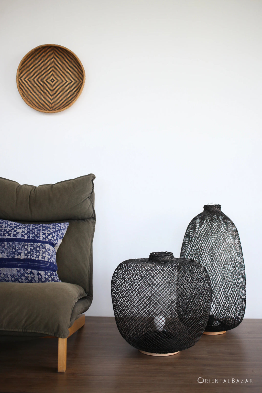 Black woven bamboo floor lamps on a wooden floor with a cushioned chair and wall art in the background.