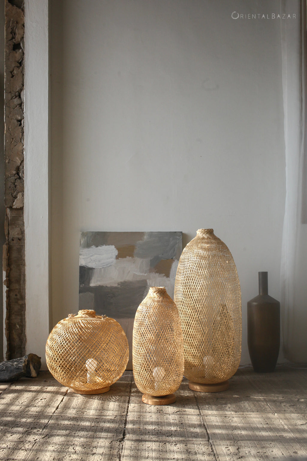 Three woven bamboo standing lamps of different sizes against a neutral wall.