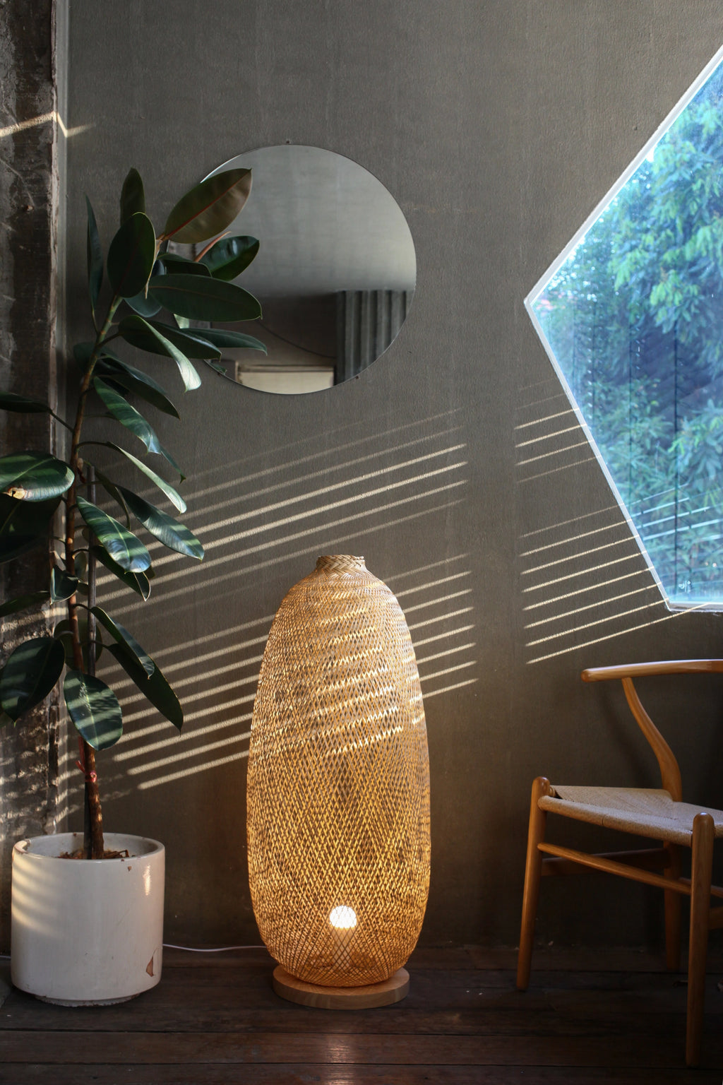 Woven bamboo floor lamp in a room with a plant and chair.