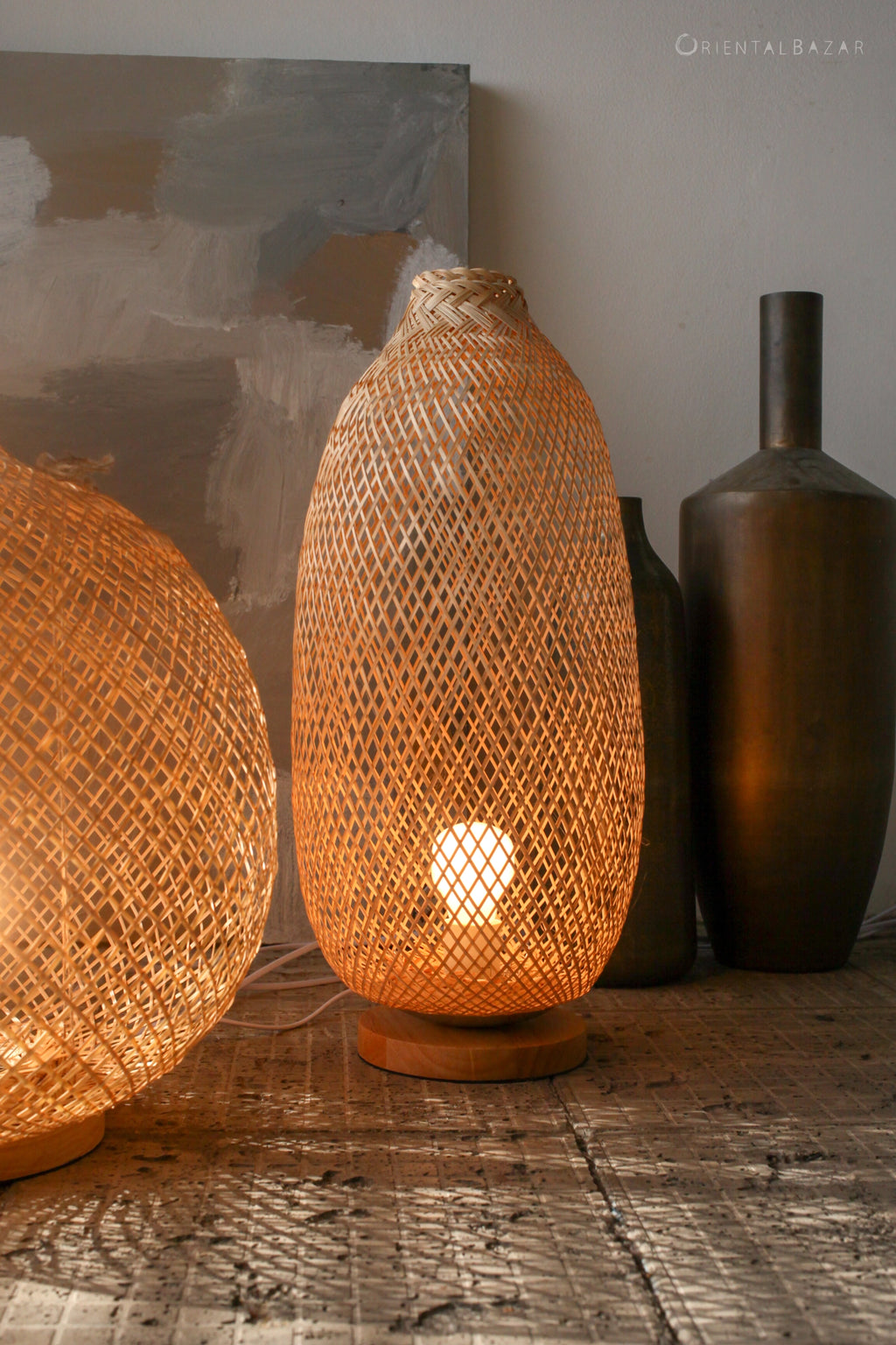 Woven bamboo standing lamp on a concrete surface with other decorative items in the background
