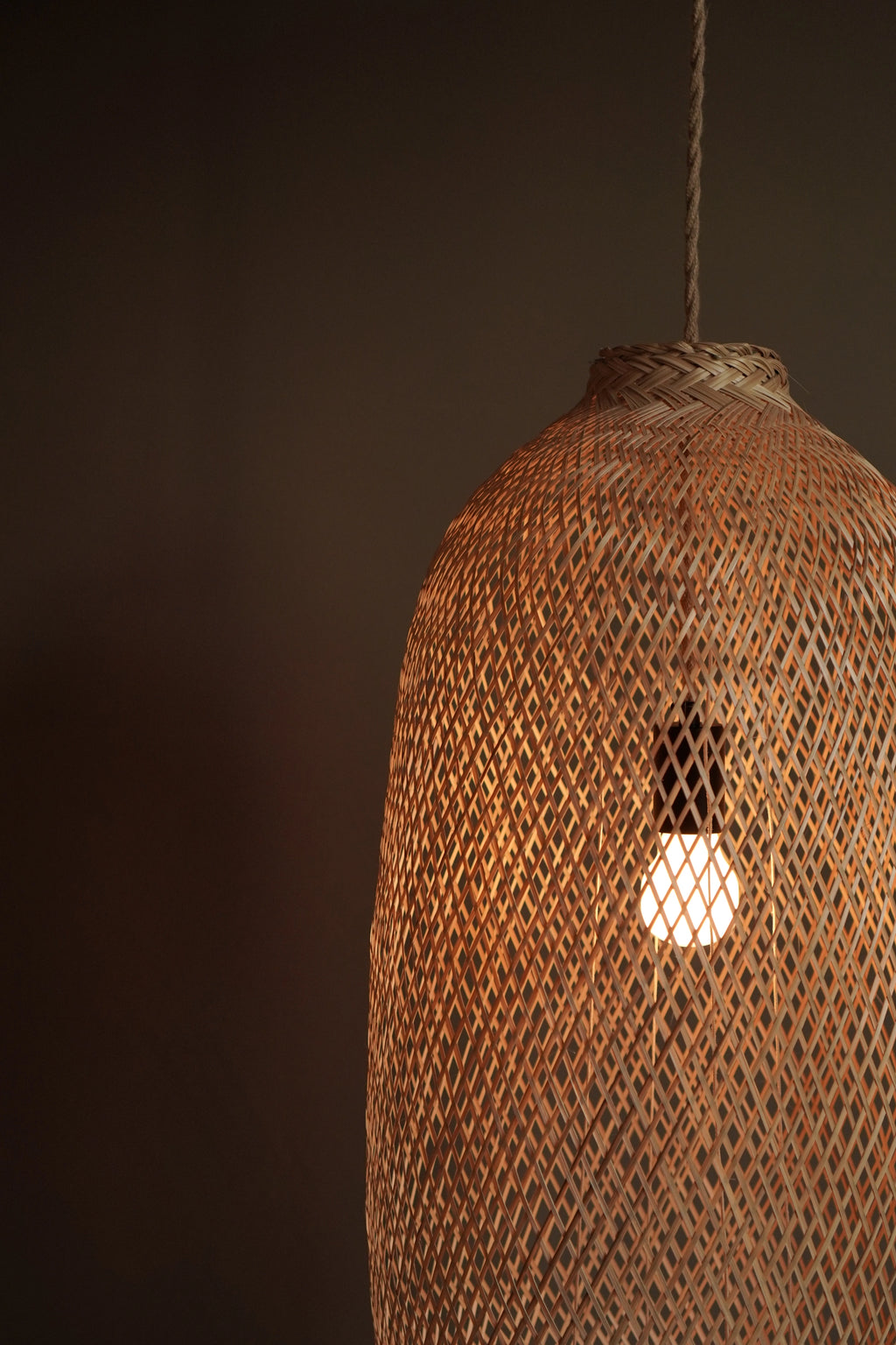 Woven bamboo pendant light with a glowing bulb against a dark background