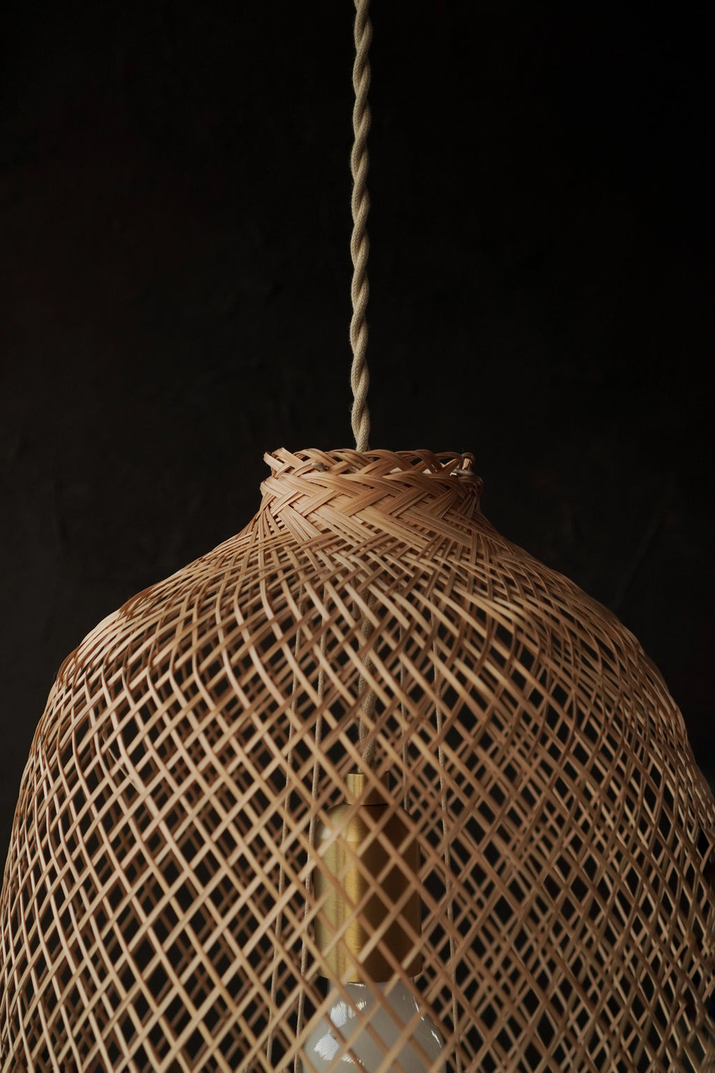 Woven rattan pendant light against a black background