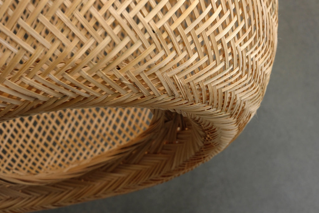 Close-up of a woven bamboo pendant light with a textured pattern on a gray background