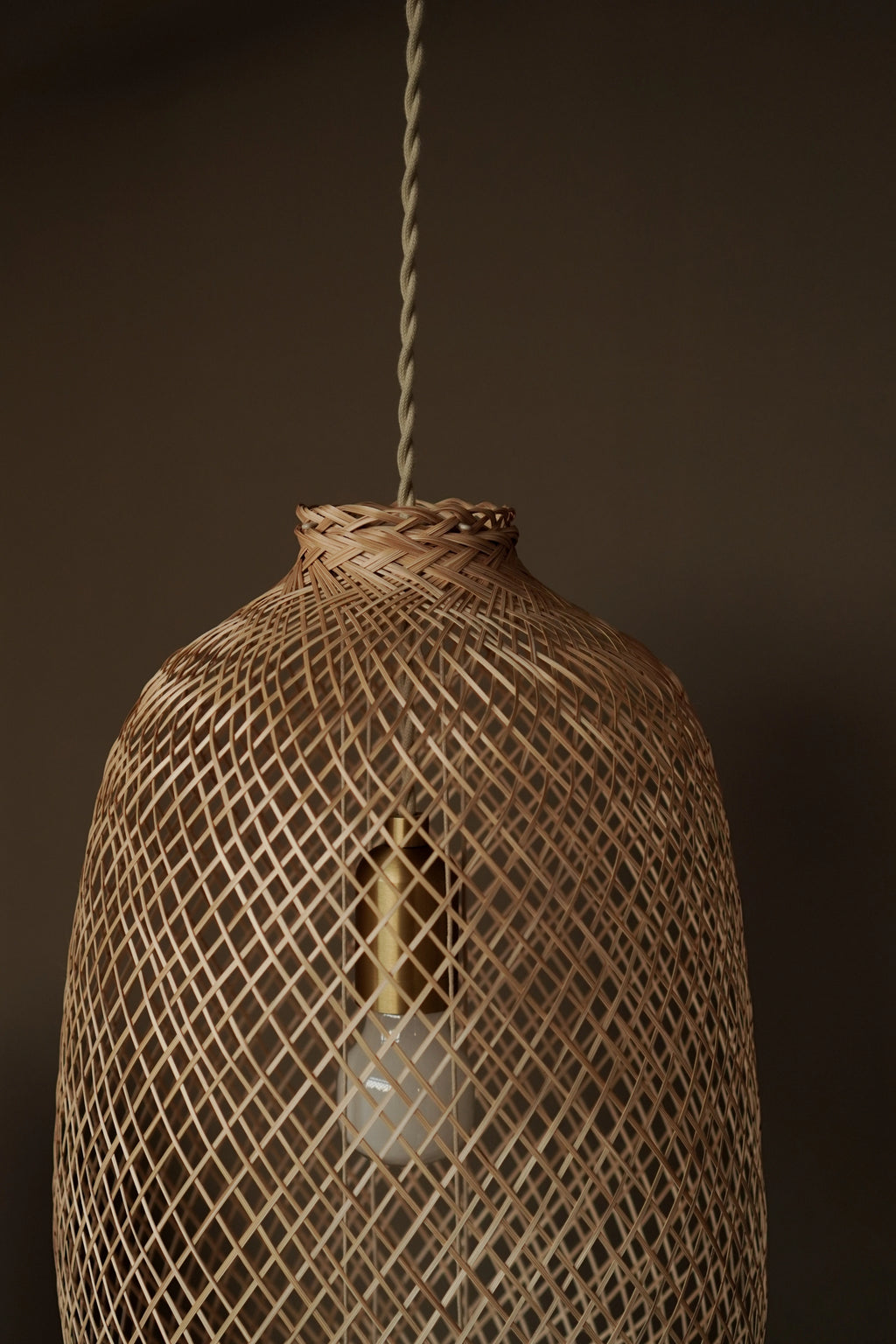 Woven bamboo light fixture with premium cord set and a bulb inside against a dark taupe background