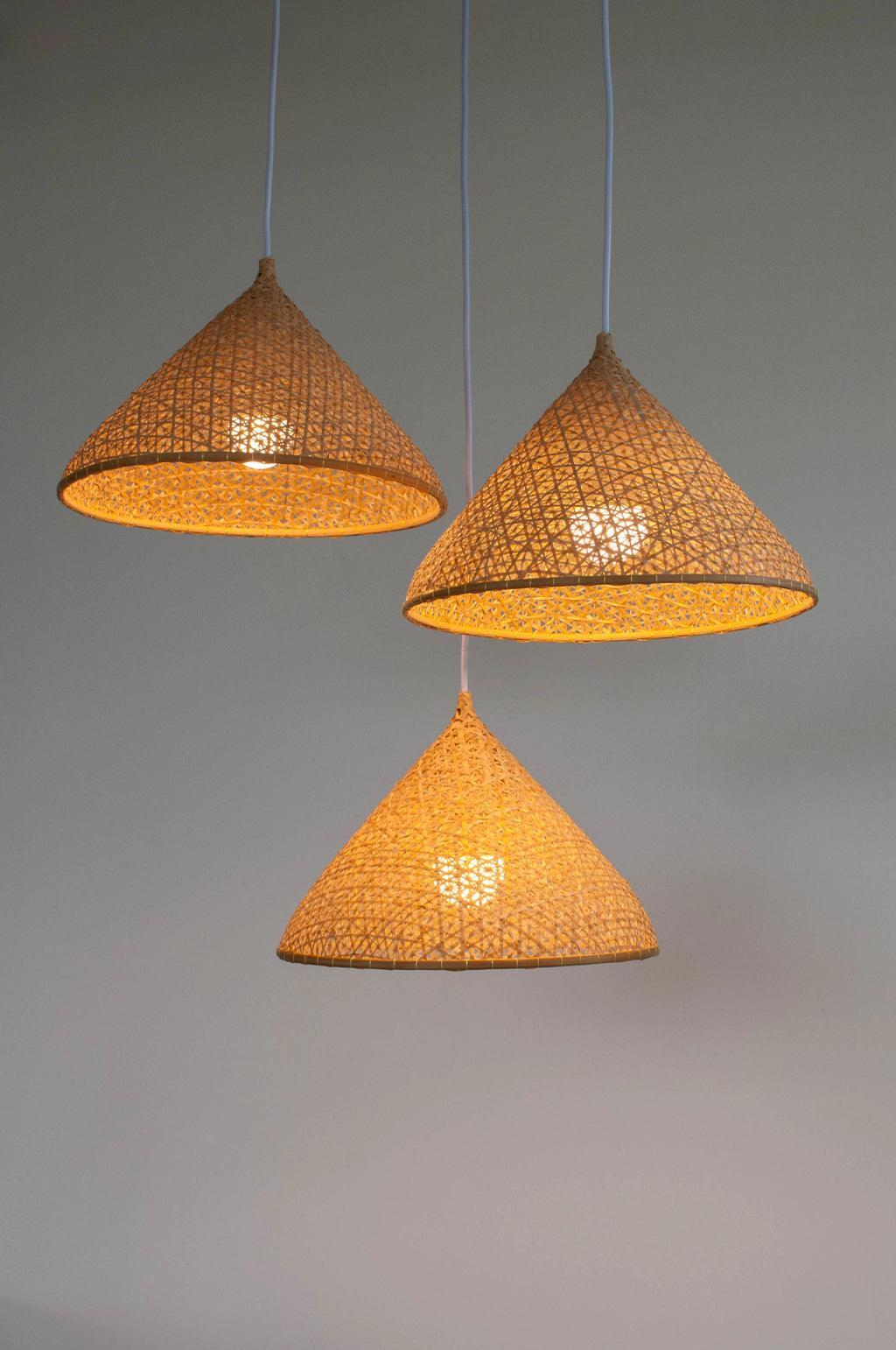 Three woven bamboo pendant lights on a gray background