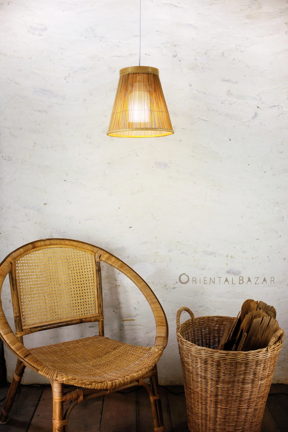Wicker chair and basket with wood against a white brick wall with a hanging bamboo lamp