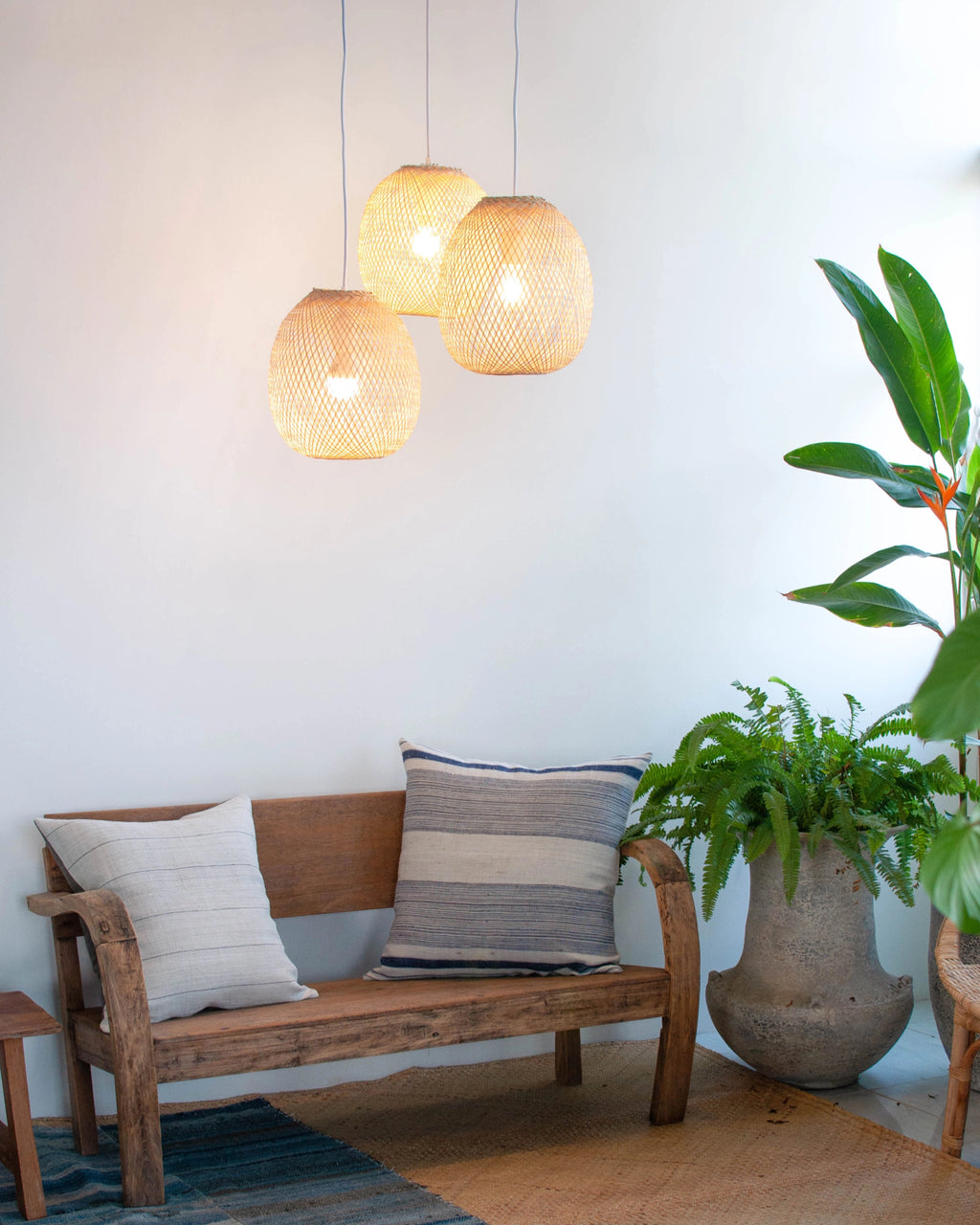 Wooden bench with cushions in a room with hanging bamboo lights and plants.