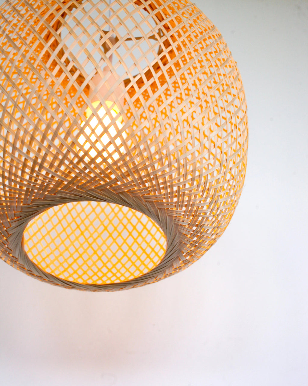 Woven bamboo pendant light with warm glow on a white background