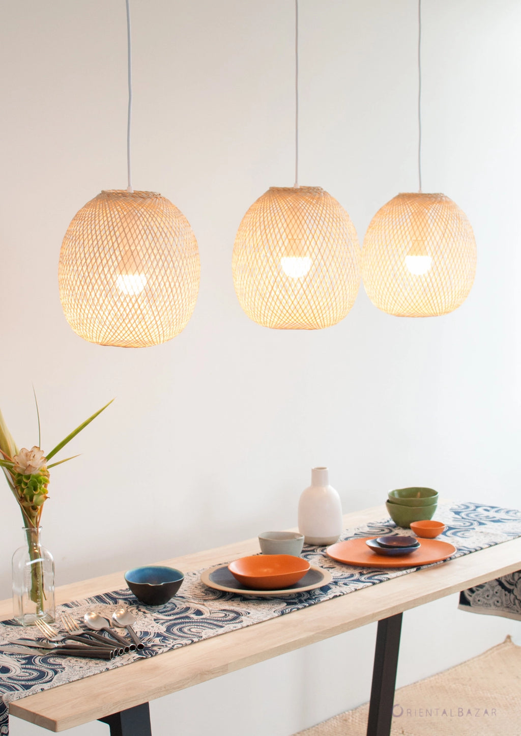 Three round woven bamboo pendant lights hanging above a dining table with a decorative tablecloth.