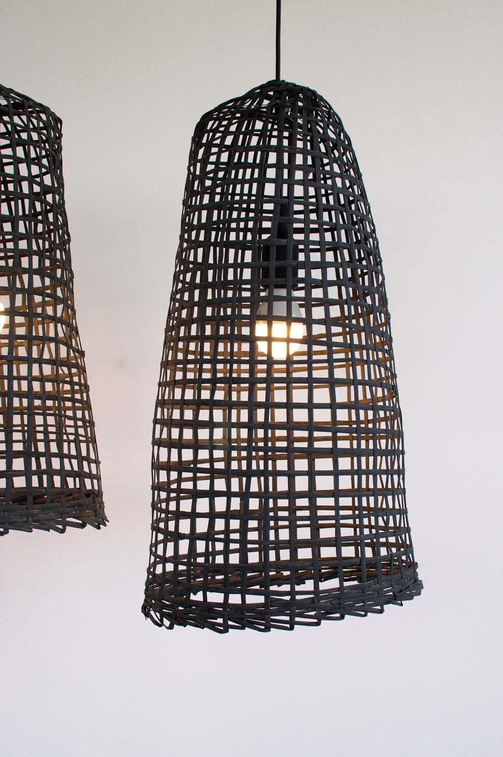 Two black bamboo woven pendant lights on a white background