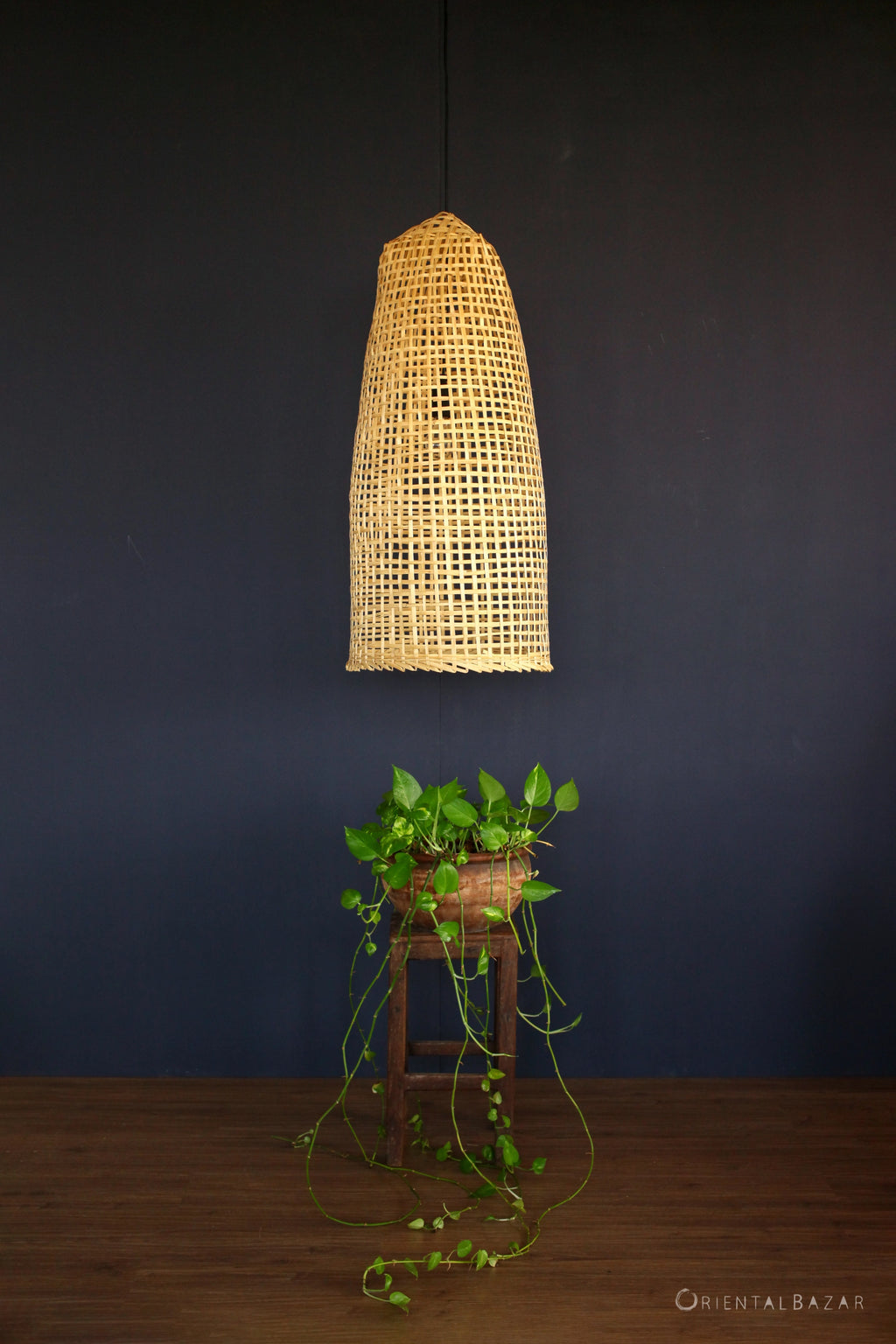 Woven bamboo ceiling light fixture on a dark wall with a plant below