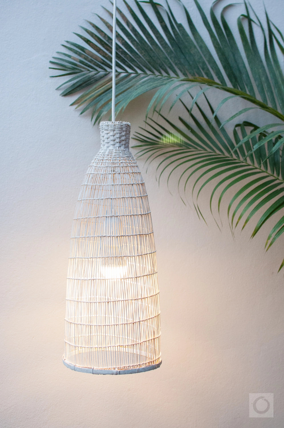 White woven pendant light with a leafy green plant in the background