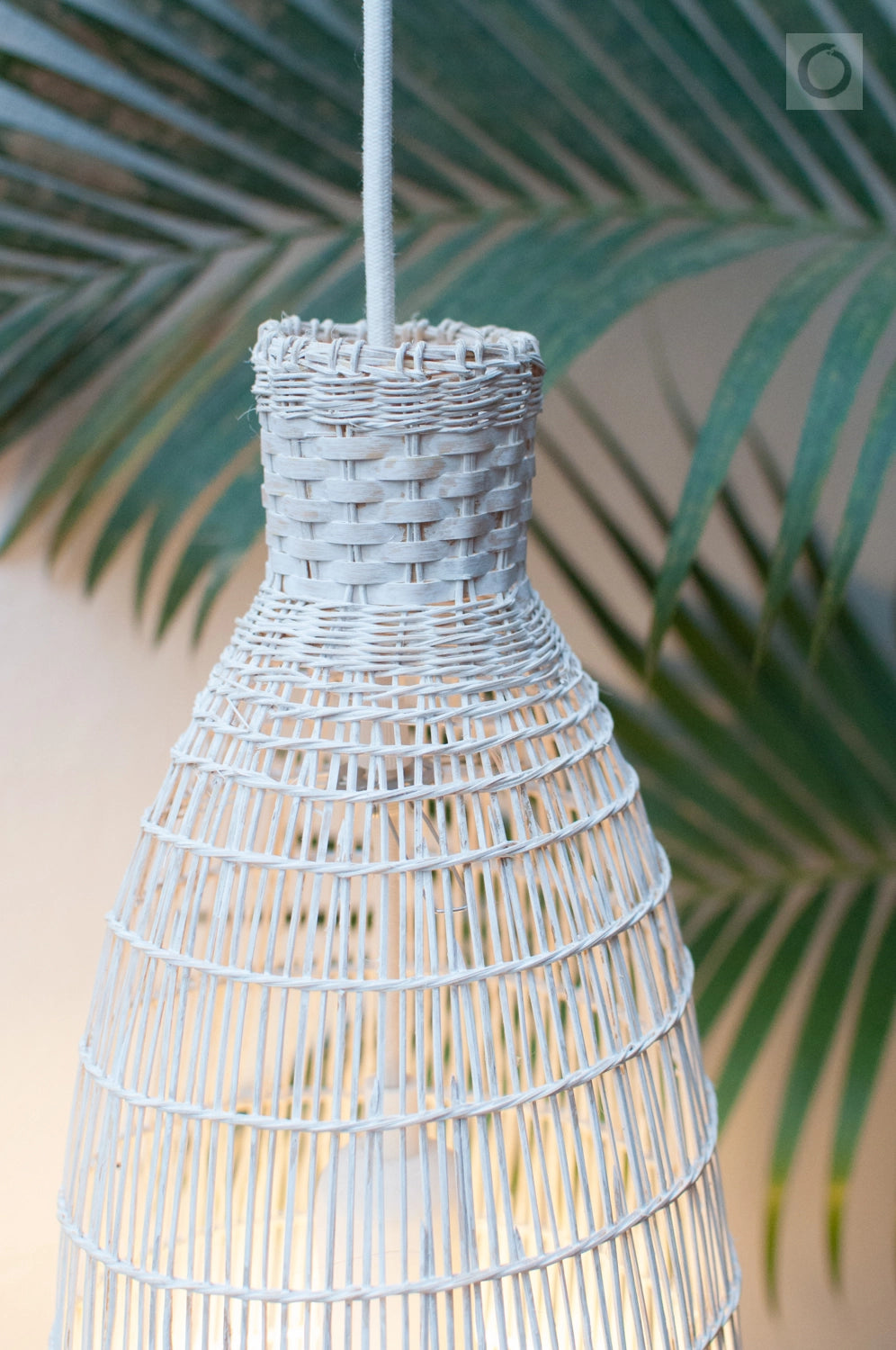 White woven bamboo pendant light with a blurred green leafy background
