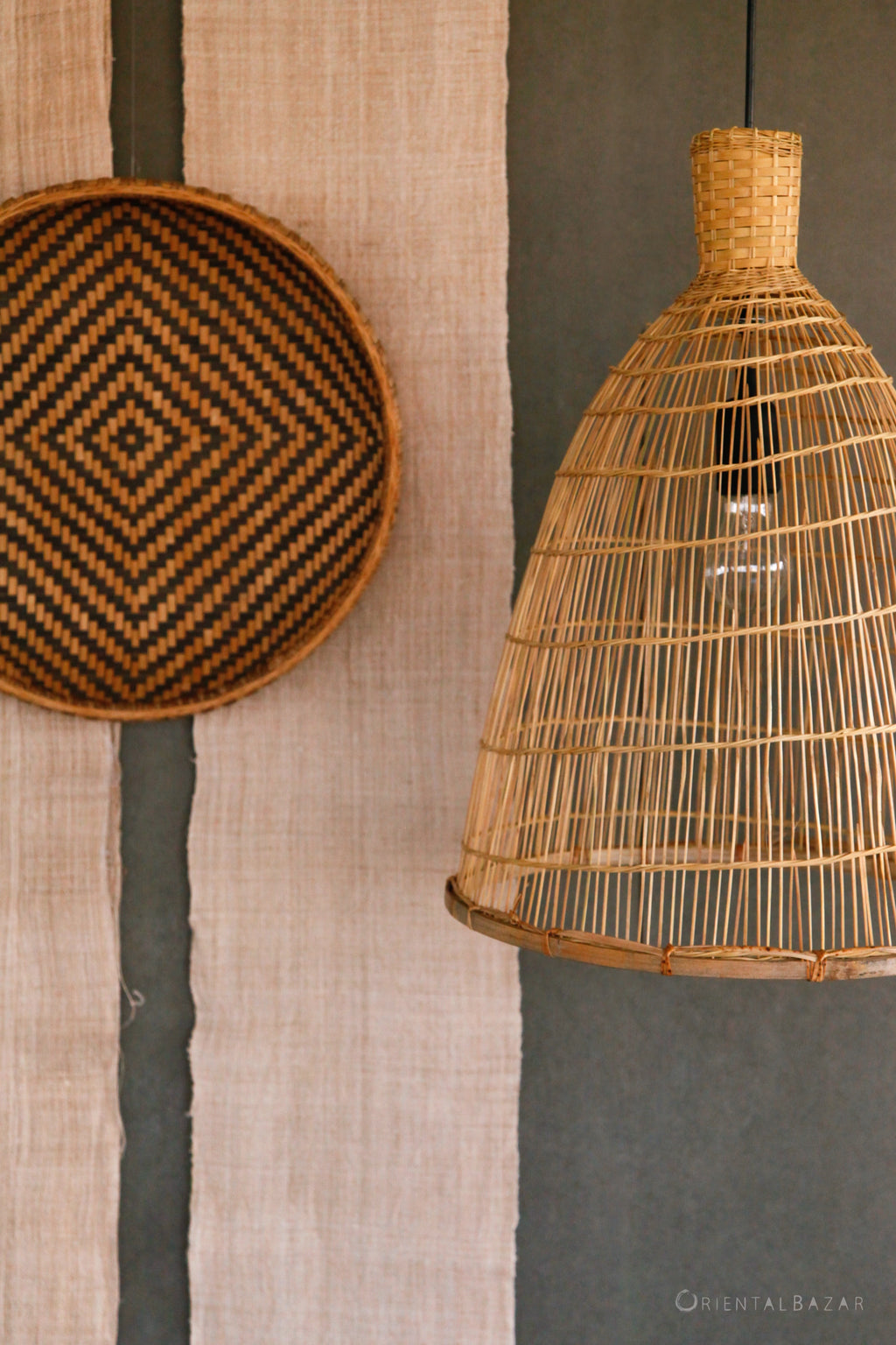 Woven bamboo and rattan pendant light hanging against a textured wall with a decorative woven basket and hanging hemp fabric
