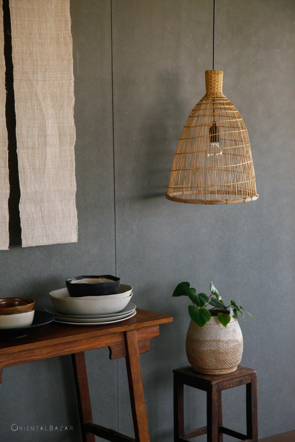 Boho bamboo lamp hanging above a wooden table with decorative items against a gray wall.